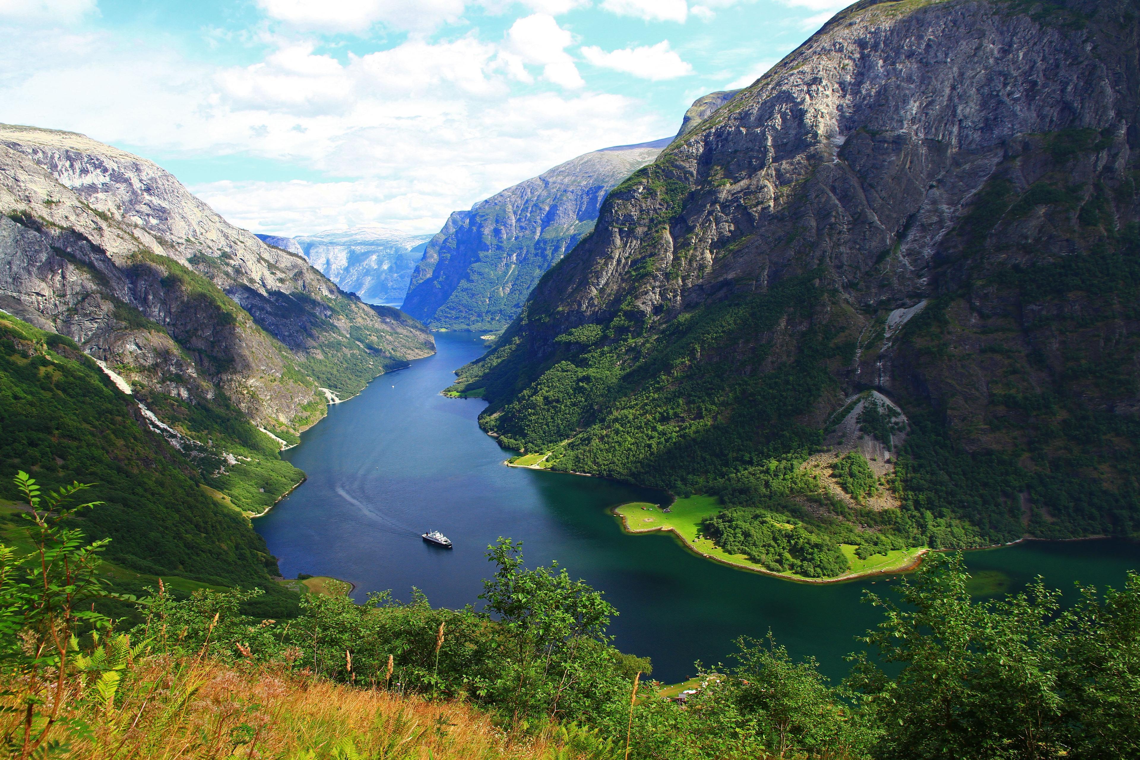 Oversiktsbilde over Nærøyfjorden og fjellene rundt. En båt kjører innover fjorden.