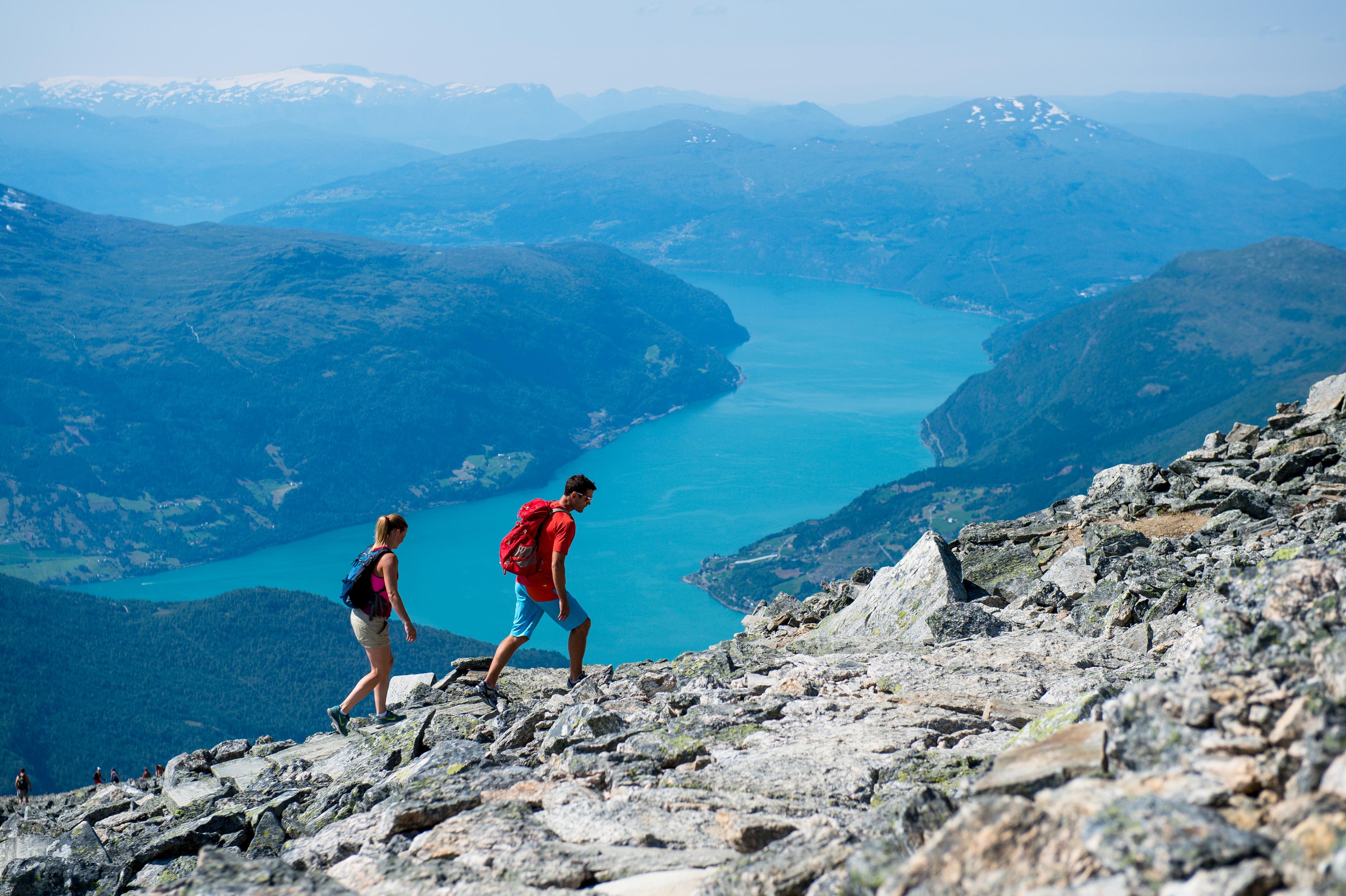 En dame og en mann på vei oppover et fjell, med utsikt ned mot fjorden.