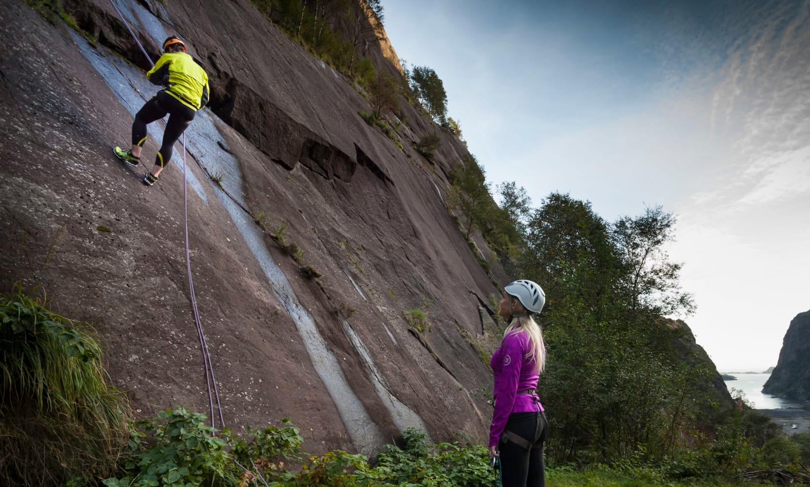 En mann klatrer og dame står i bunn av fjell og ser på klar for å klatre - Klatring Jøssingfjord